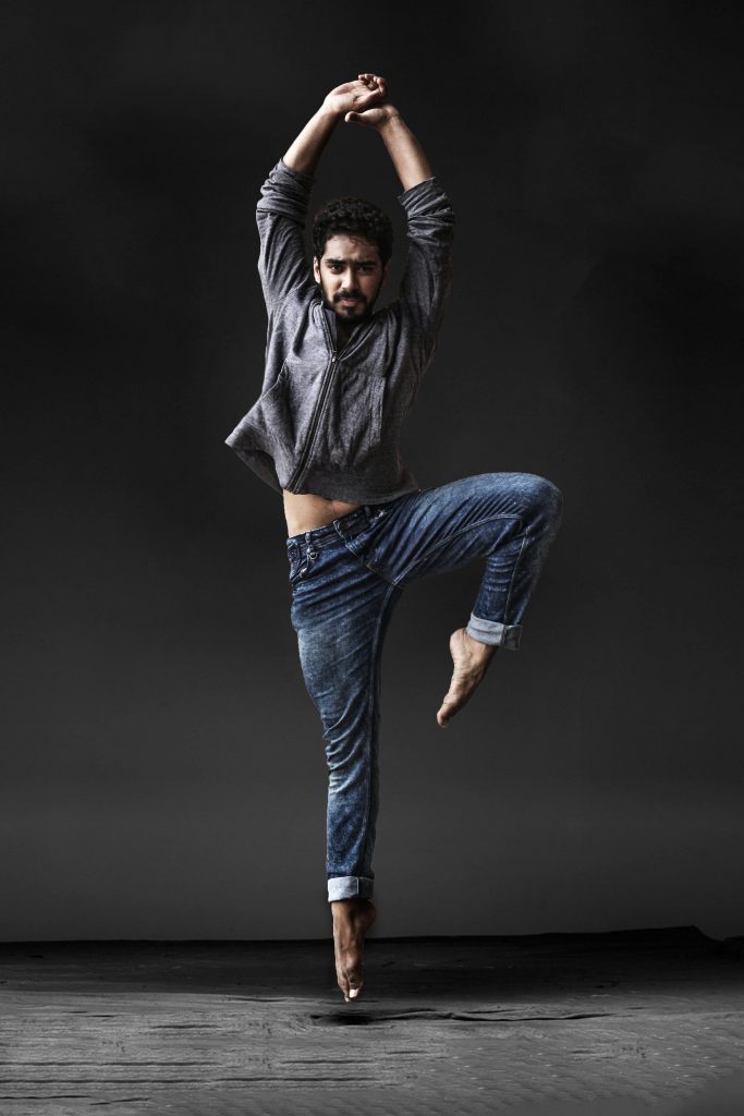 A male dancer performs a dramatic contemporary dance pose against a dark background, showcasing athleticism and elegance.