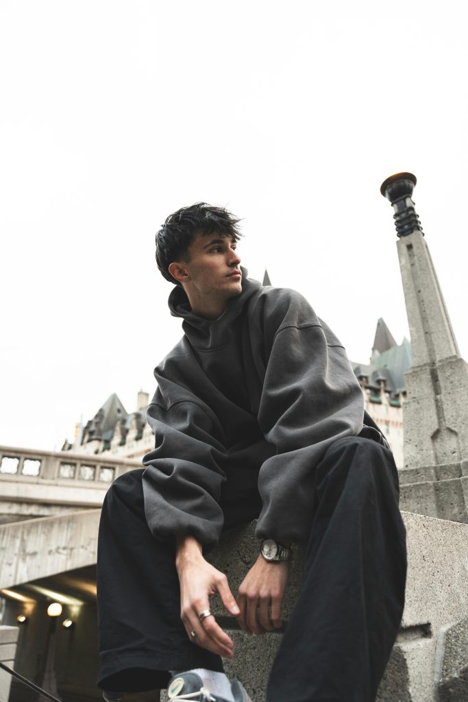 Young man in a hoodie sitting by gothic architecture. Urban fashion.