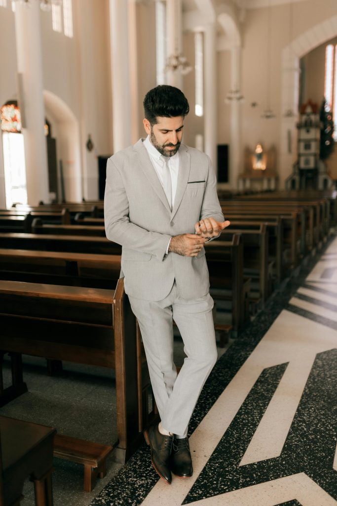 Man in a stylish suit stands in a beautifully designed church interior checking his phone.