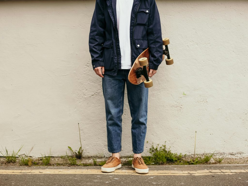 Young man holding skateboard against urban wall, showcasing casual street style.